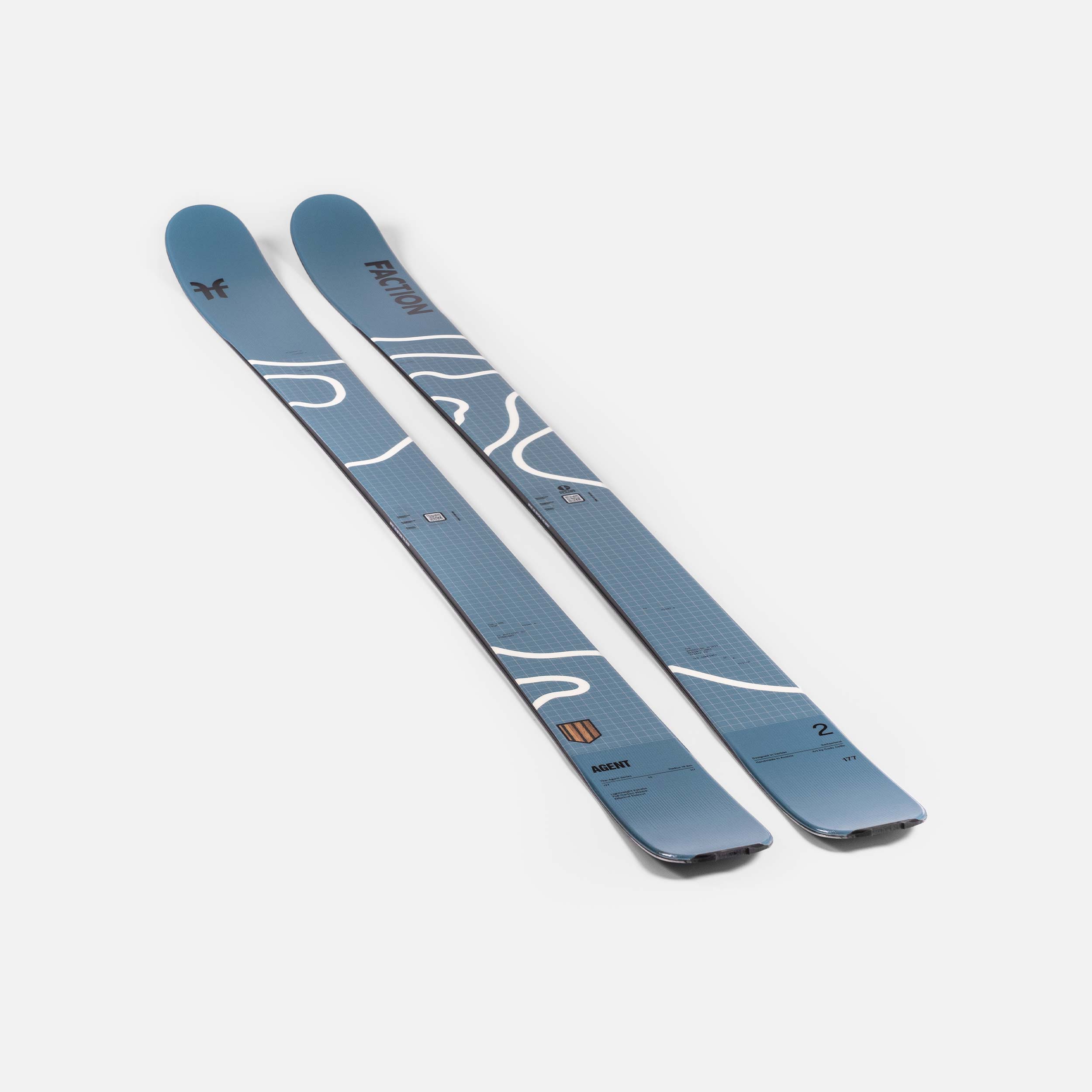 Zwei blaue Faction Ski mit weißem Muster liegen diagonal auf einem weißen Untergrund.