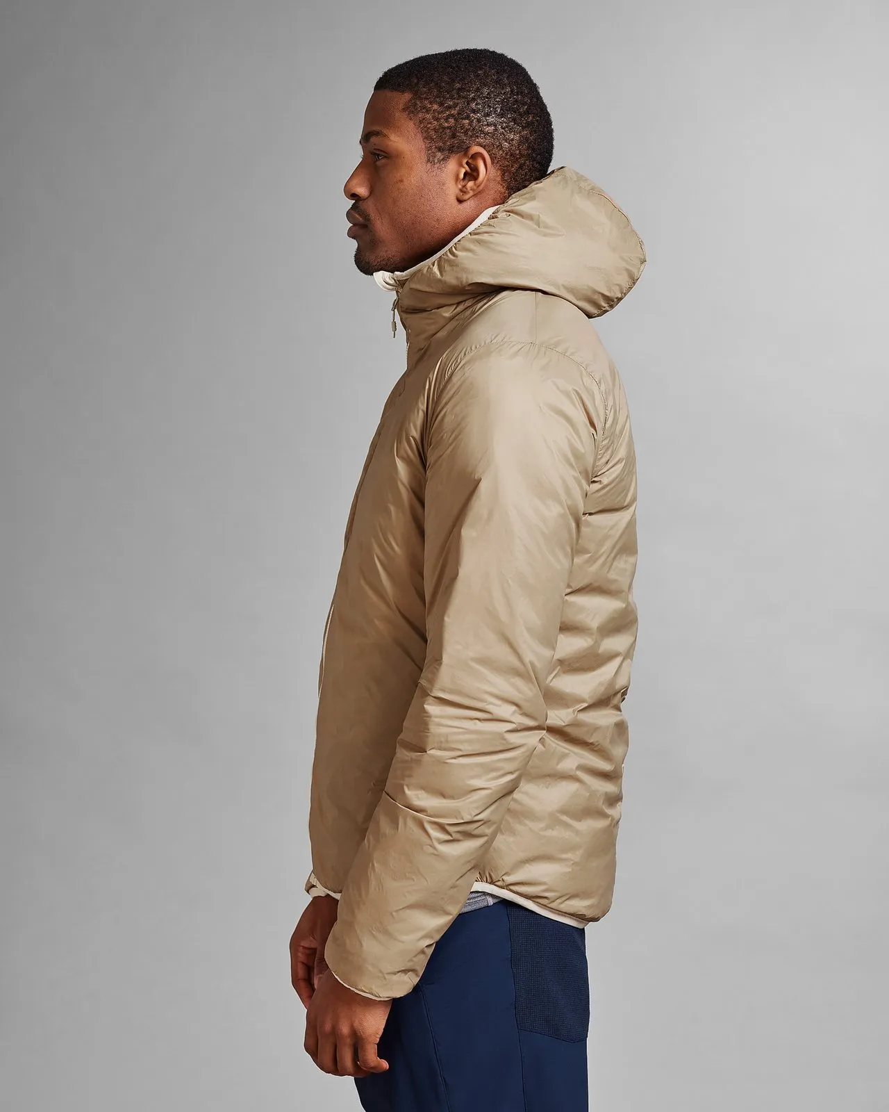 A man wears a reversible, light brown D-3L Light Hood jacket in profile against a gray background.