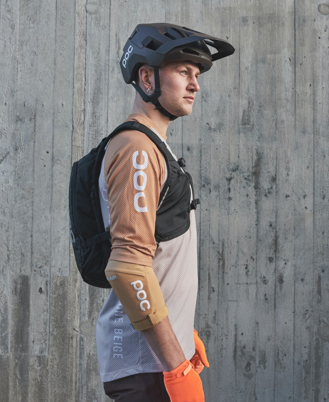 Mann mit VPD Rucksack Ein Mann mit Helm und Column VPD Backpack 13L vor einer Betonwand, Seitenansicht.
