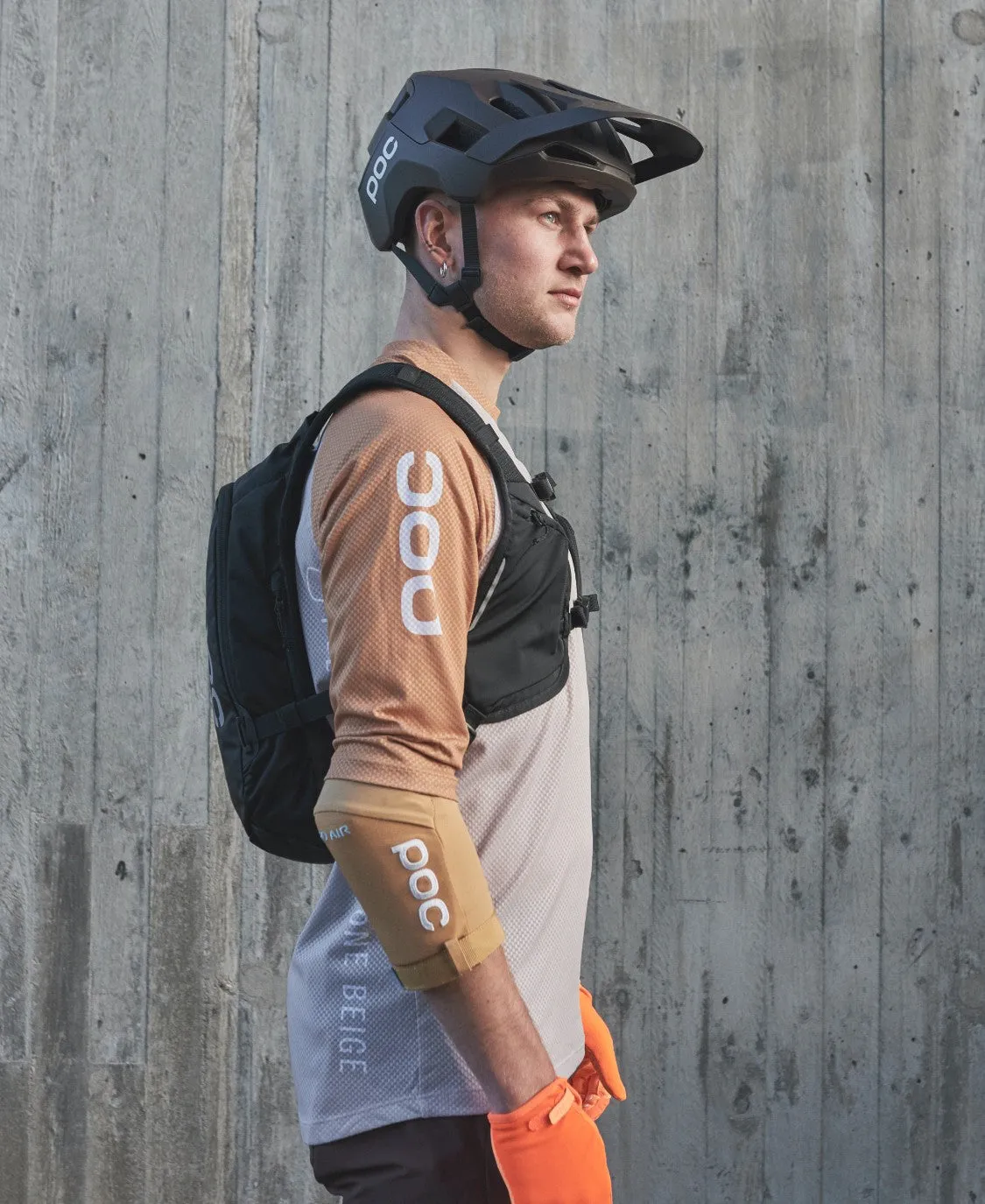 Ein Mann mit Helm und Column VPD Backpack 13L vor einer Betonwand, Seitenansicht.