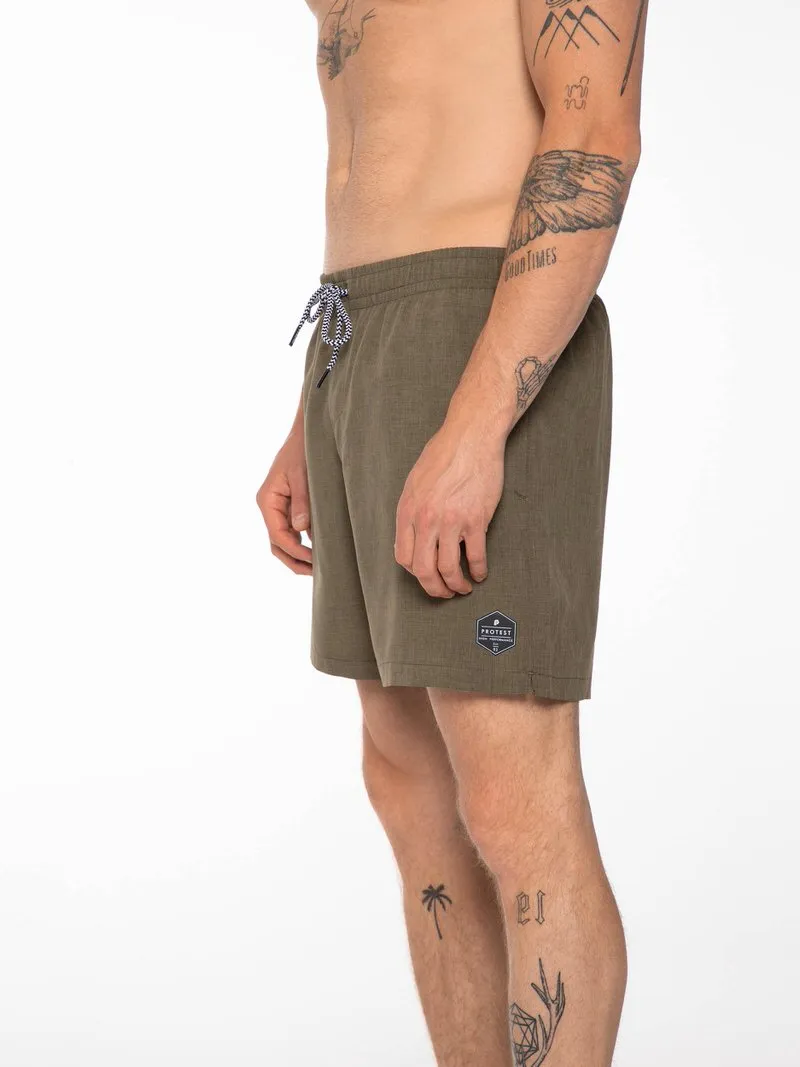 A man in green swim shorts with drawstring and "Protest" logo, side view, tattoos on arms and legs.