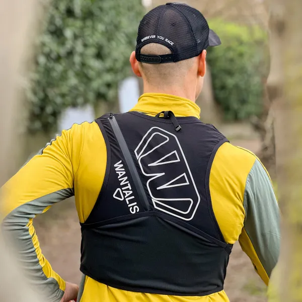 Coureur avec gilet d'hydratation Hydrabag Elite 8L vu de dos, casquette noire avec impression, t-shirt jaune à manches longues, vue sur la nature.