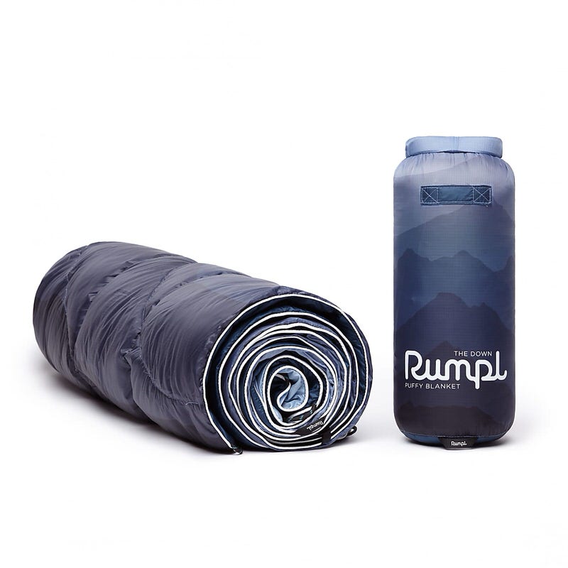 Gerollte, blaue Rumpl Down Puffy Decke und ein passender Packsack mit Bergen im Hintergrund.