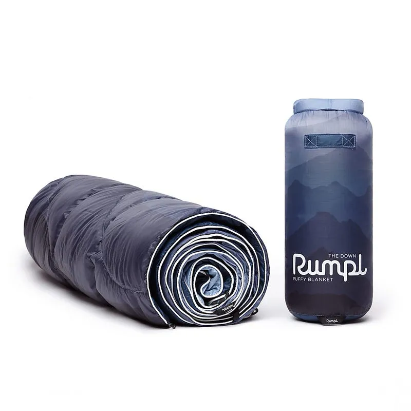 Gerollte, blaue Rumpl Down Puffy Decke und ein passender Packsack mit Bergen im Hintergrund.