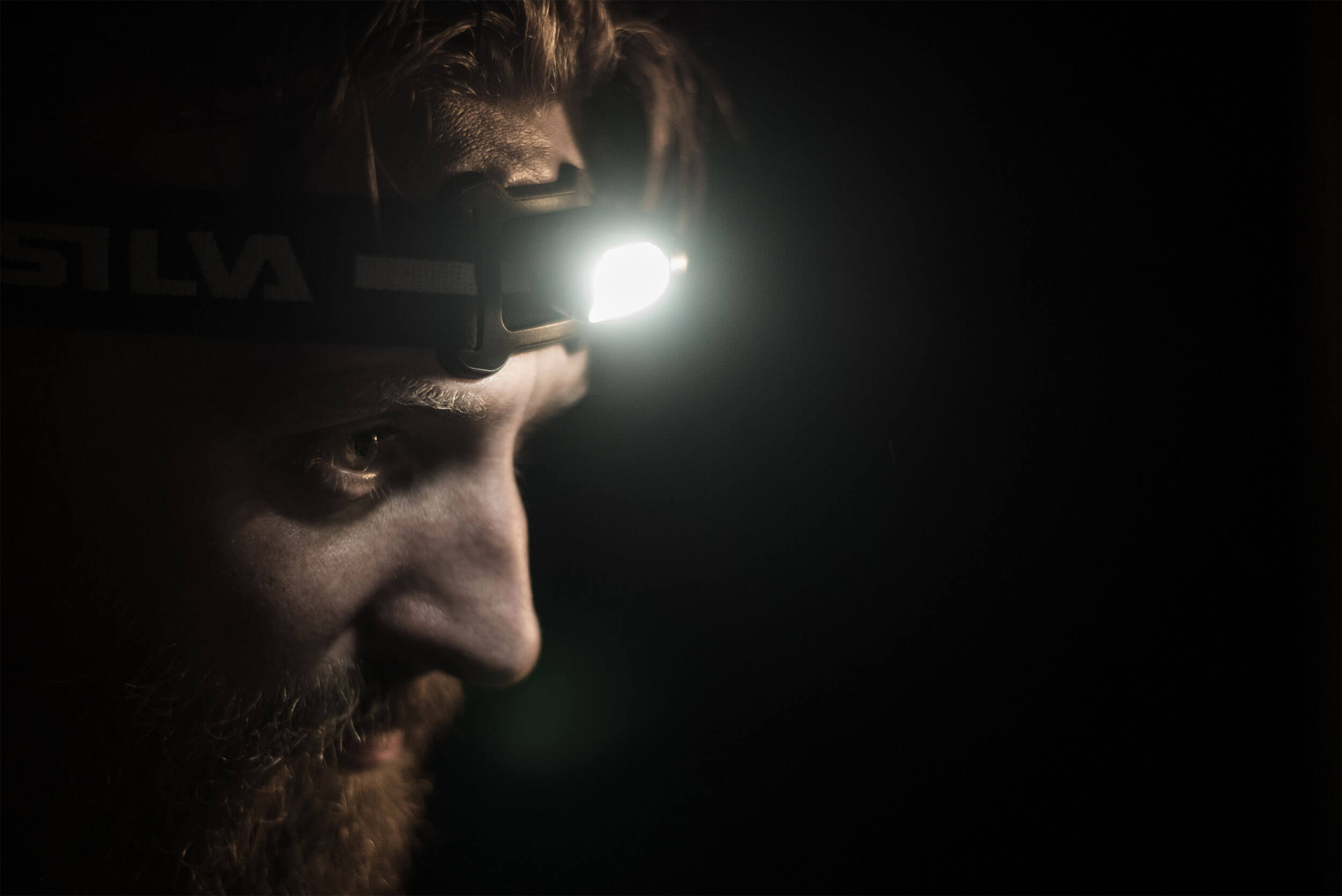 Profil d'un homme avec une barbe portant une lampe frontale Silva Scout 3 allumée.