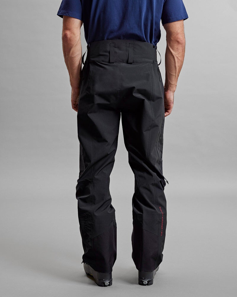 Rückansicht GORE-TEX Hose Rückansicht: Person mit schwarzer Y-1 HD GORE-TEX Pro 3L Shell Pant, Hose mit Reißverschlüssen und dezentem Markenlogo.
