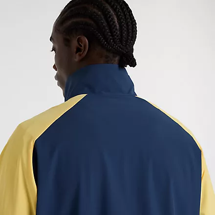New Balance Track Jacket Nahaufnahme einer New Balance In Game Woven Track Jacket in Navy/Gelb, getragen von einem Mann. Die Jacke hat einen Stehkragen.