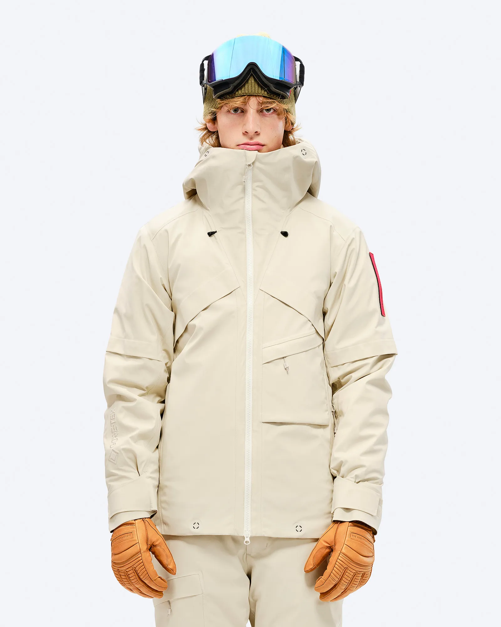 Man in ski jacket and trousers. Beige S-1 GORE-TEX 2L Stretch Insulated Jacket, gloves and ski goggles.