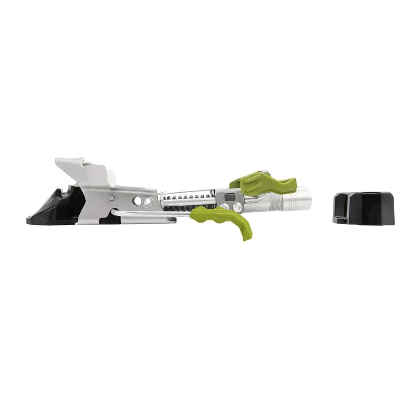 Fixation de ski de randonnée métallique argentée sur fond blanc, de profil. Leviers vert olive et pièces en plastique noir aux extrémités, réglages et ressorts visibles. À côté, une pièce noire séparée.