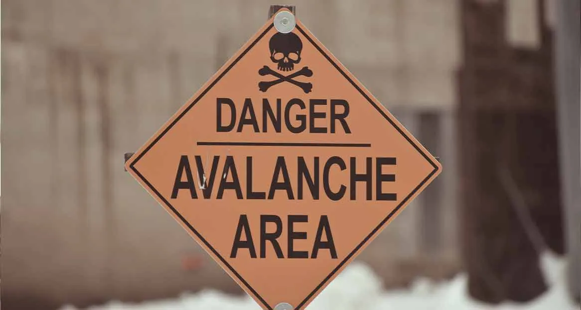 An orange, diamond-shaped warning sign with black lettering "DANGER AVALANCHE AREA" and a skull symbol.
