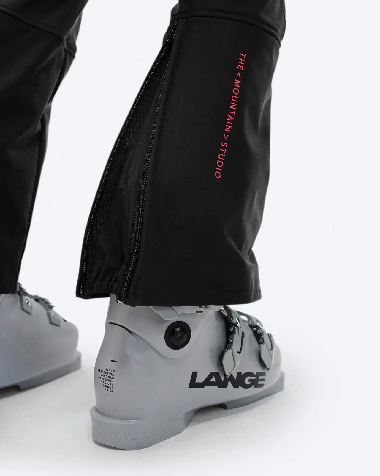Nahaufnahme einer schwarzen Stretch-Skihose über einem grauen Skischuh mit Reißverschluss und Markenlogo.