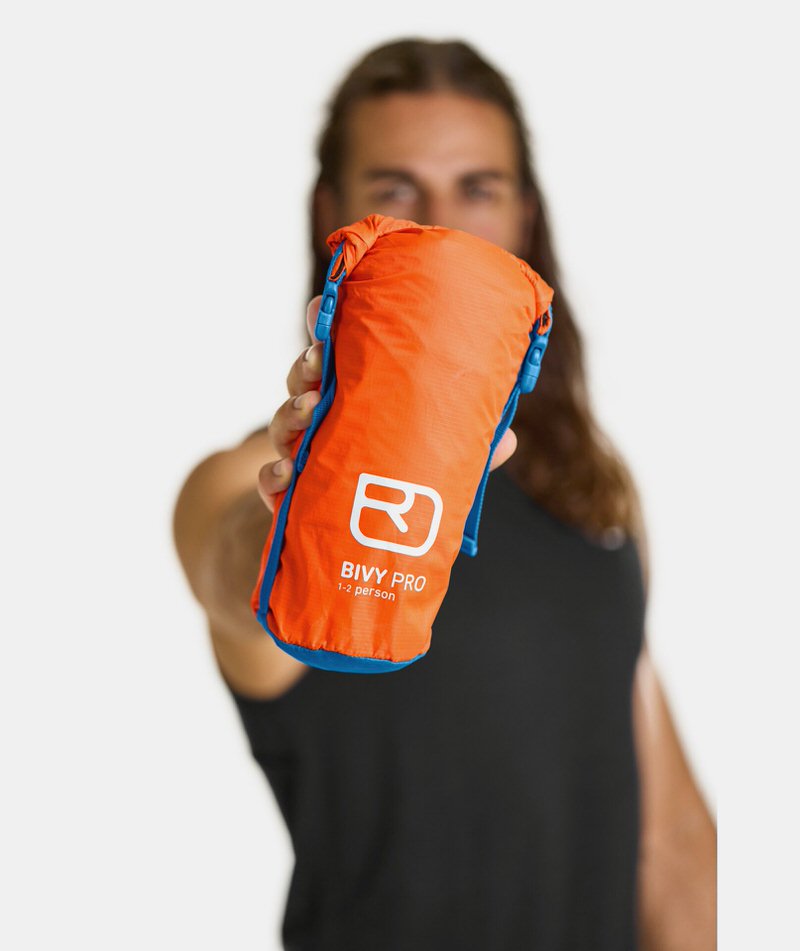 Orangefarbener Ortovox Bivy Pro Biwaksack, kompakt verpackt, in einer Hand gehalten.