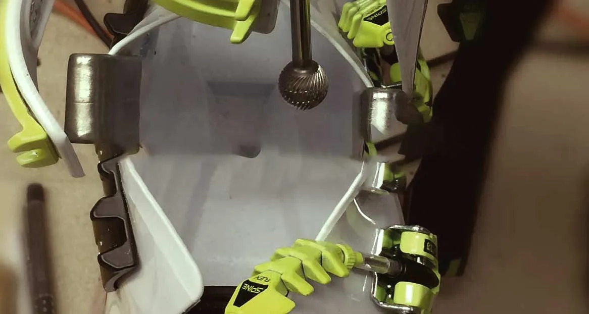 Interior view of a ski boot with fitting tool and yellow Spine Flex elements. Metal parts and plastic elements are visible.