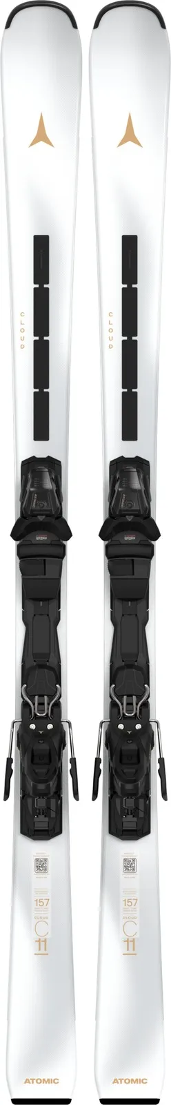 Two white skis with black bindings are standing vertically next to each other. Golden markings and lettering can be seen on the skis.