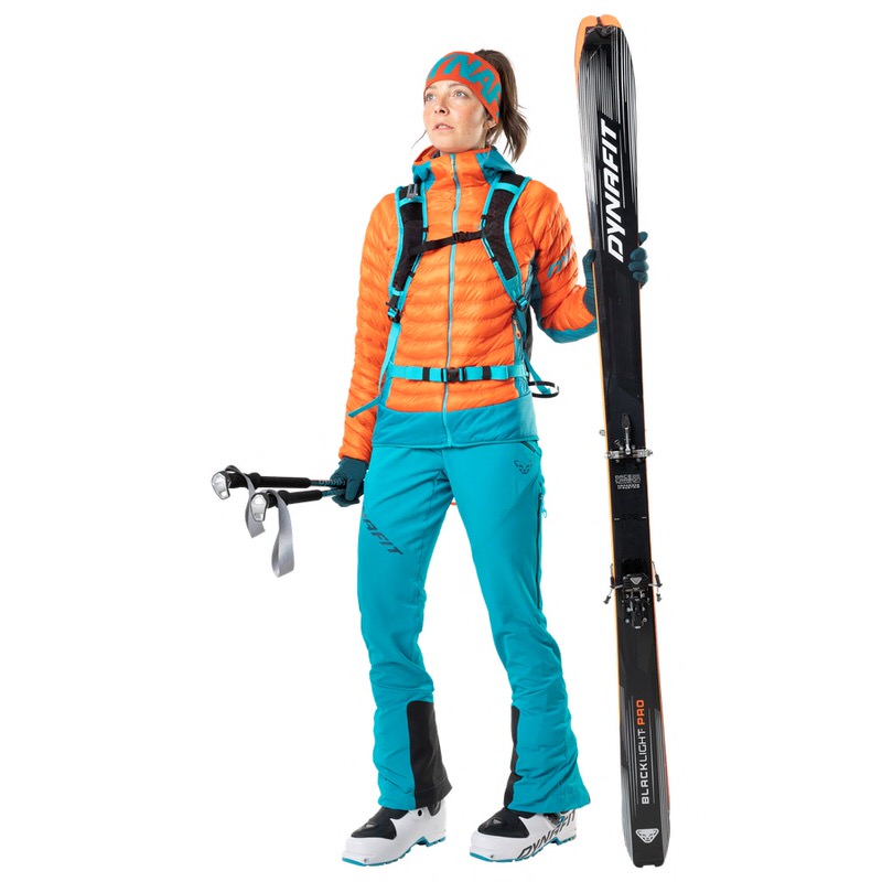 Frau in Skikleidung mit Skiern und Stöcken. Sie trägt eine petrolfarbene Dynafit TLT Touring Hose.