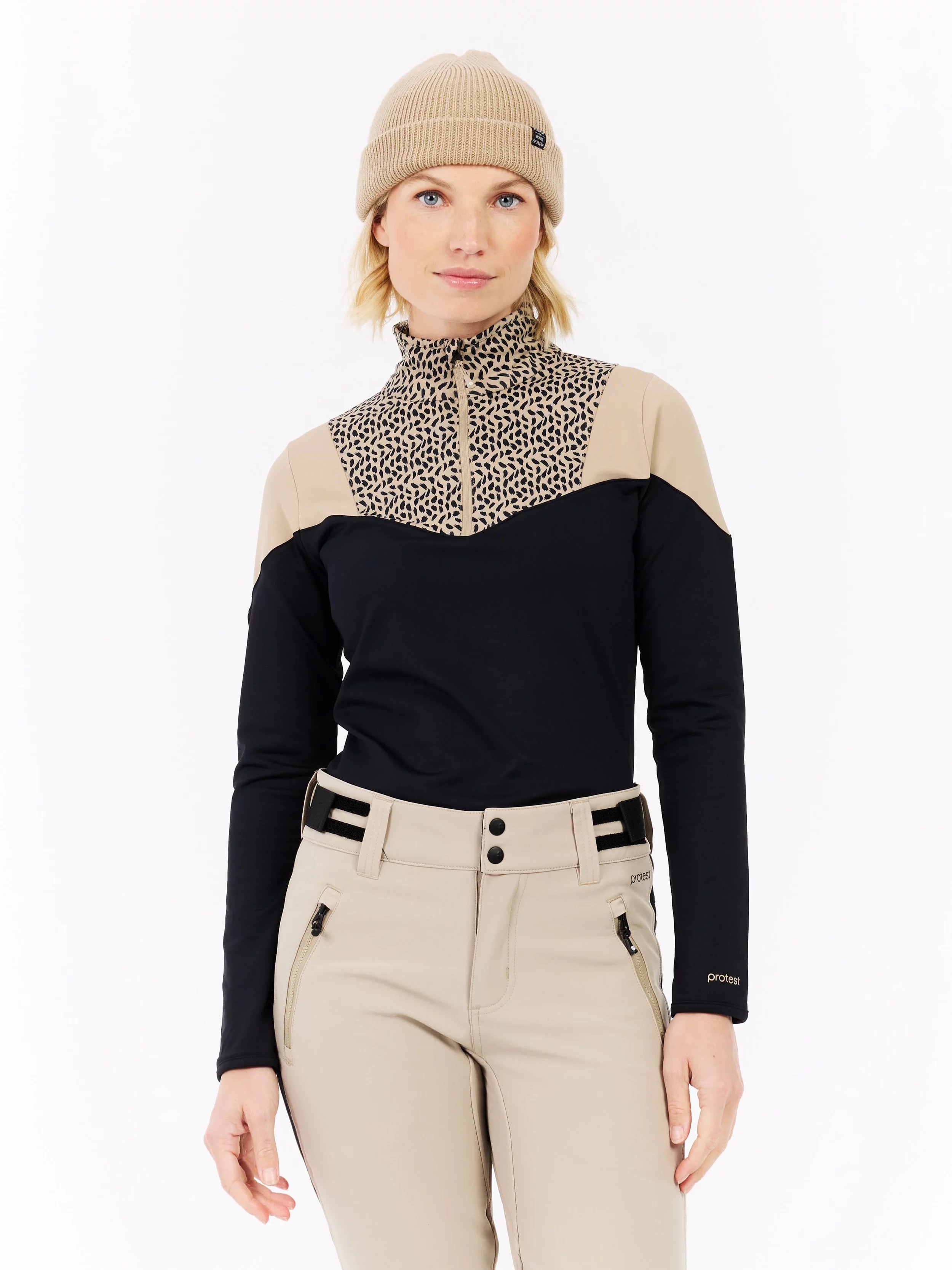 Woman with cap wears leopard print top with black sleeves and beige pants.