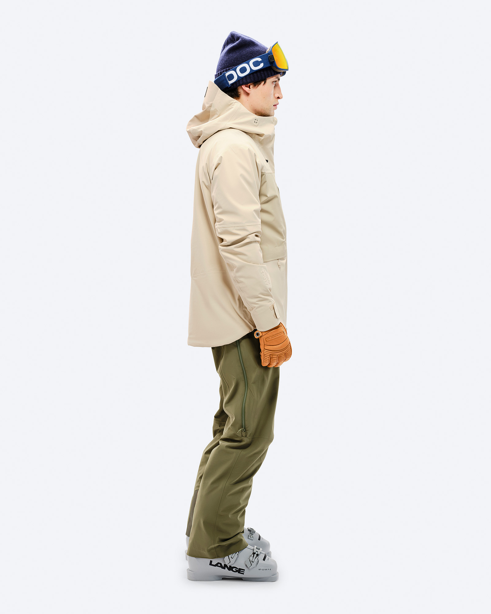 Mann in Ski-Ausrüstung Ein Mann in Ski-Ausrüstung von der Seite: Beige Jacke, grüne Hose, Skischuhe, Mütze und Brille.