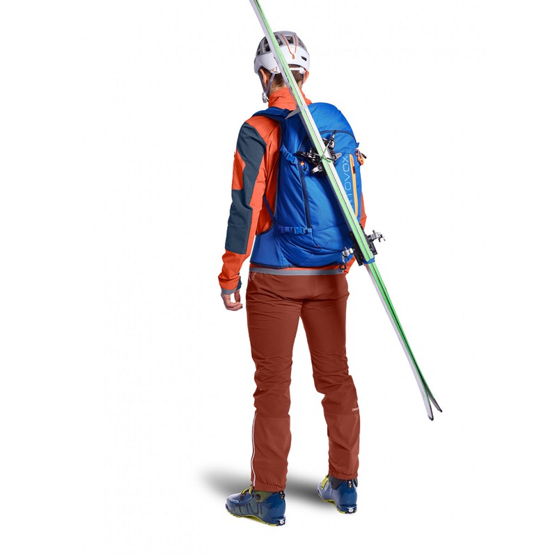 Skifahrer mit Ortovox Rucksack Person mit Skiern und blauem Ortovox Tour Rider 28 S Rucksack, von hinten. Ski sind am Rucksack befestigt.