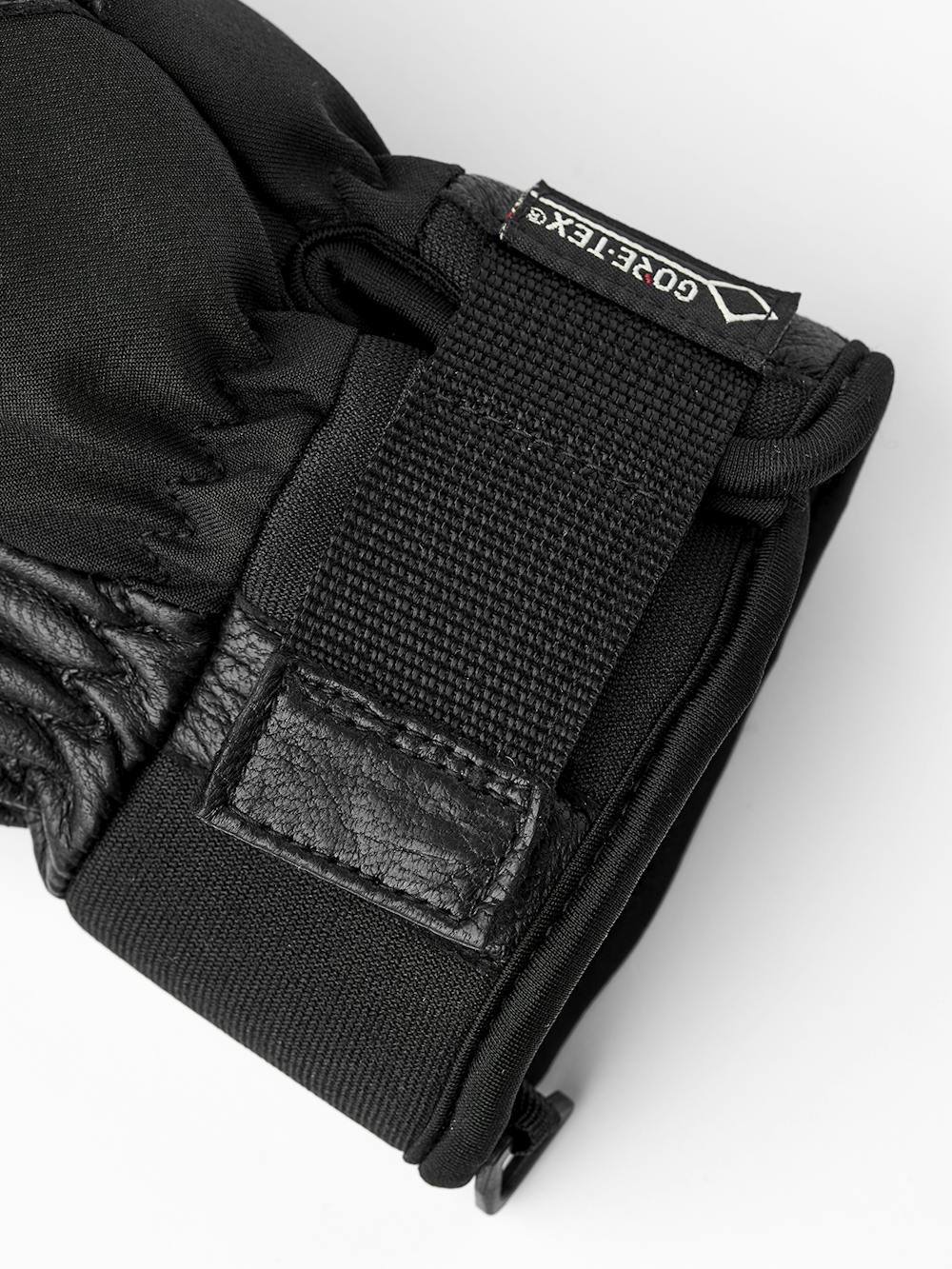 Detailaufnahme eines schwarzen Handschuhs mit Lederdetails und einem GORE-TEX® Etikett.