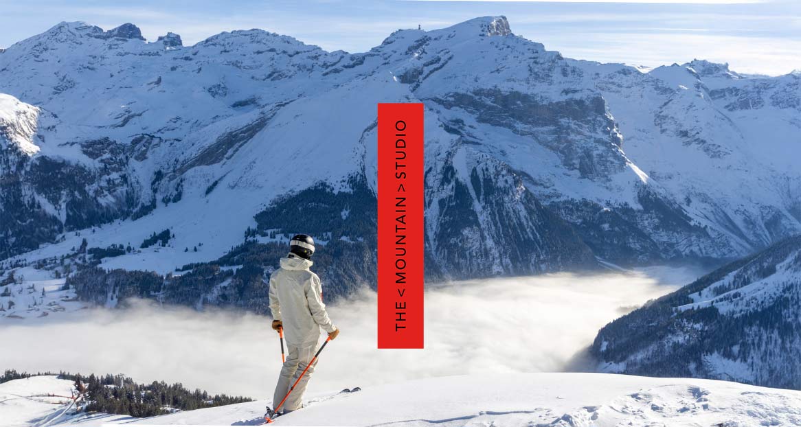 Skifahrer vor verschneiten Bergen, mit Nebel im Tal. Roter Balken mit dem Text: "THE STUDIO".