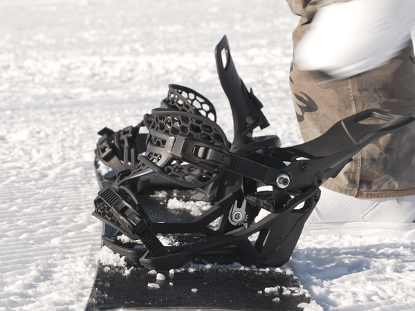 Schwarze Snowboardbindung im Schnee Schwarze Snowboardbindung auf einem Snowboard im Schnee, im Hintergrund eine Person.