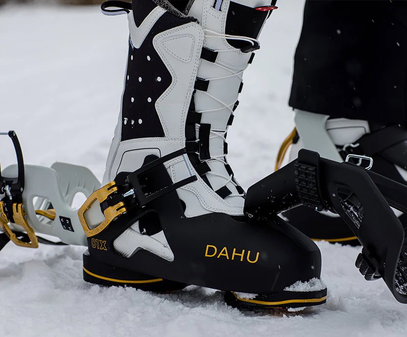 DAHU Skischuhe Schwarz-Weiß Schwarze und weiße DAHU Skischuhe mit goldfarbenen Akzenten und Bindungen im Schnee.