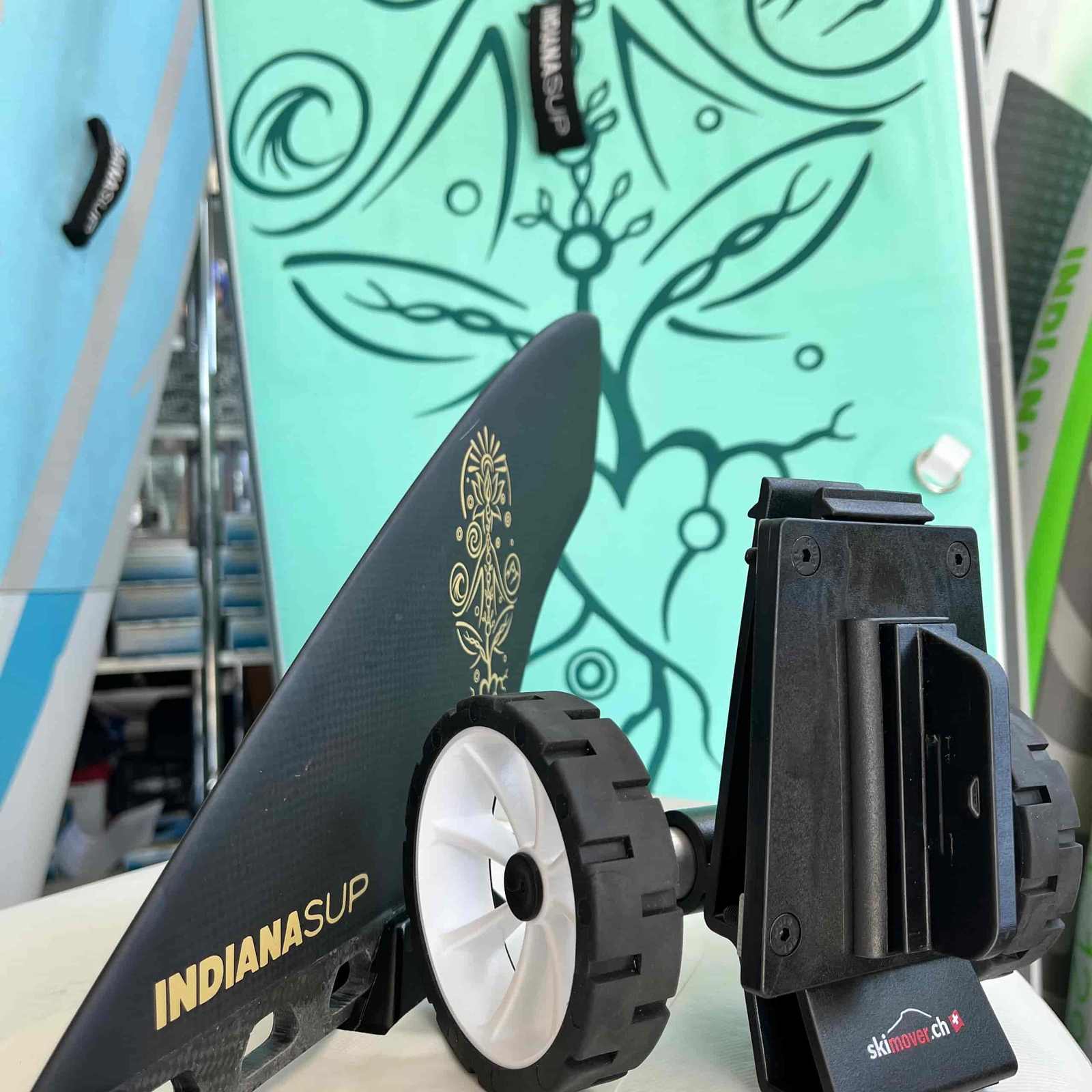 SUPmover wheels, with black holder, white rim, next to a fin and a SUP board.