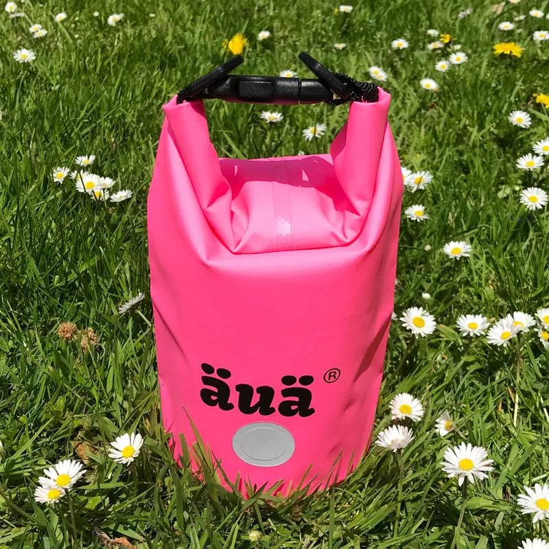 Pinker wasserdichter Packsack der Marke äuaä, platziert im grünen Gras mit Gänseblümchen.
