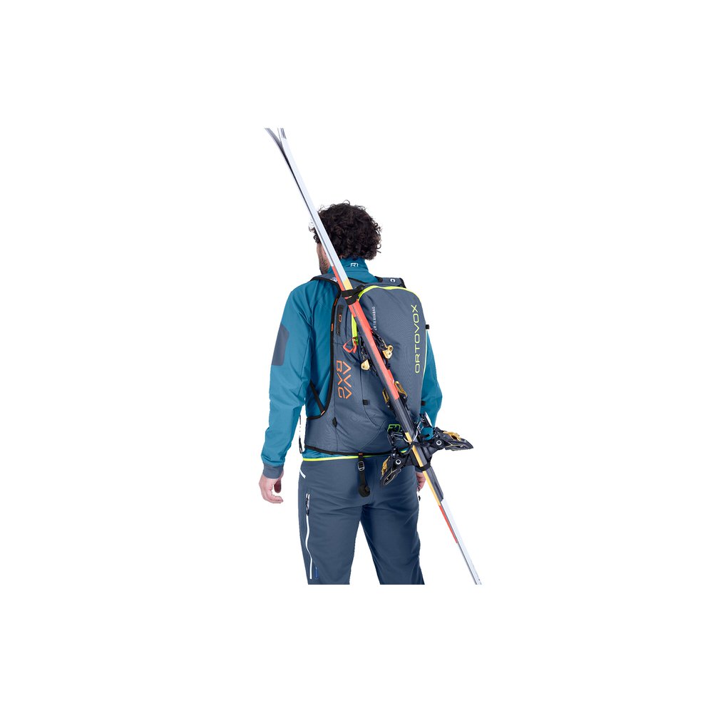 Personne avec un sac à dos gris Cross Rider 18 pour les avalanches et des skis fixés en diagonale depuis l'arrière.