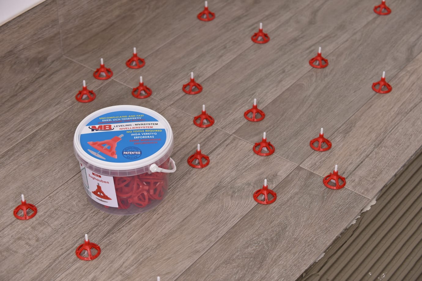 Carrelage avec système de nivellement Capots de tirage et languettes. Seau avec housses de tirage au premier plan. Hottes de traction rouges réparties sur les carreaux.