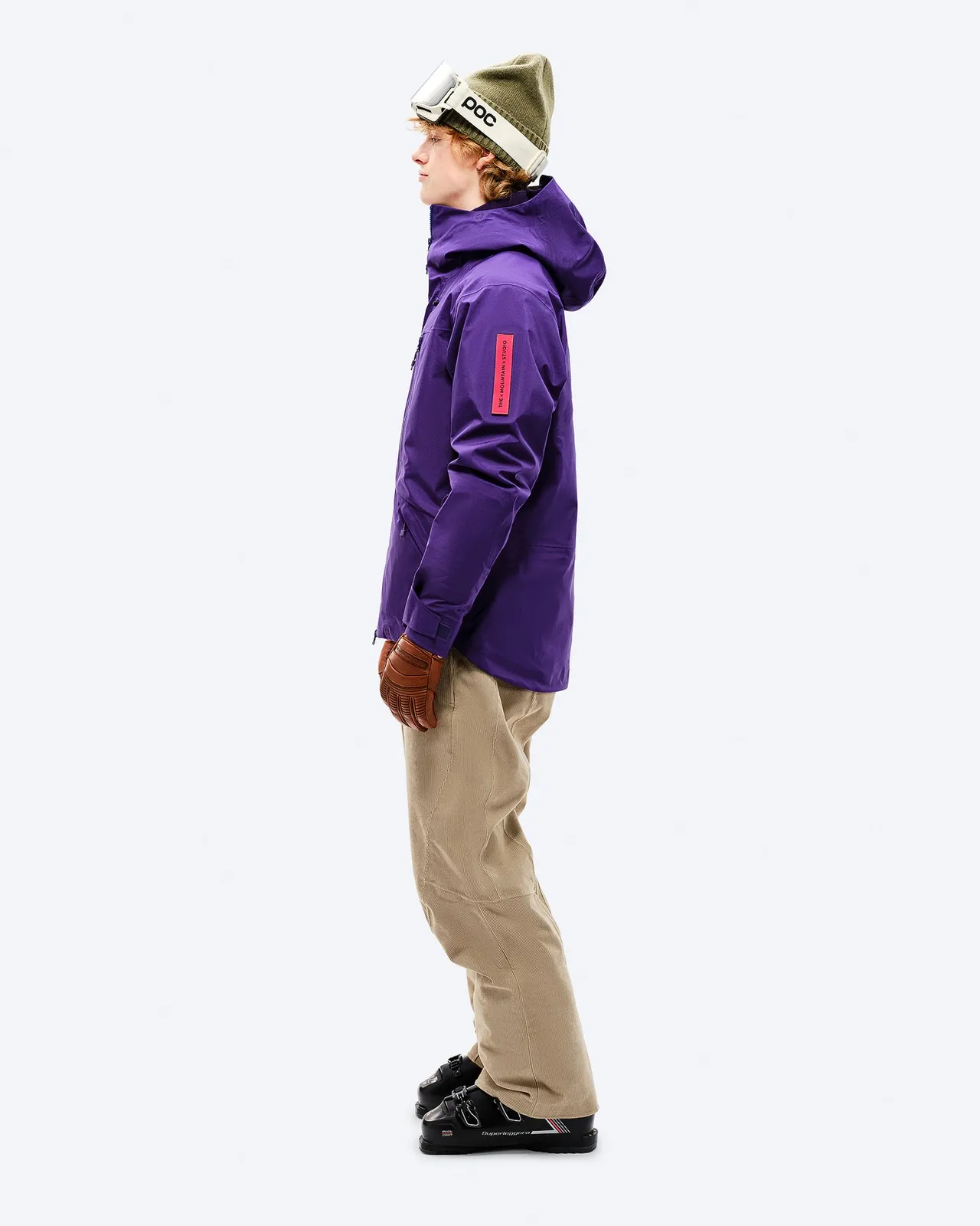 Person in purple GORE-TEX EPE 3L Shell Jacket, ski pants, gloves and ski boots, side view.