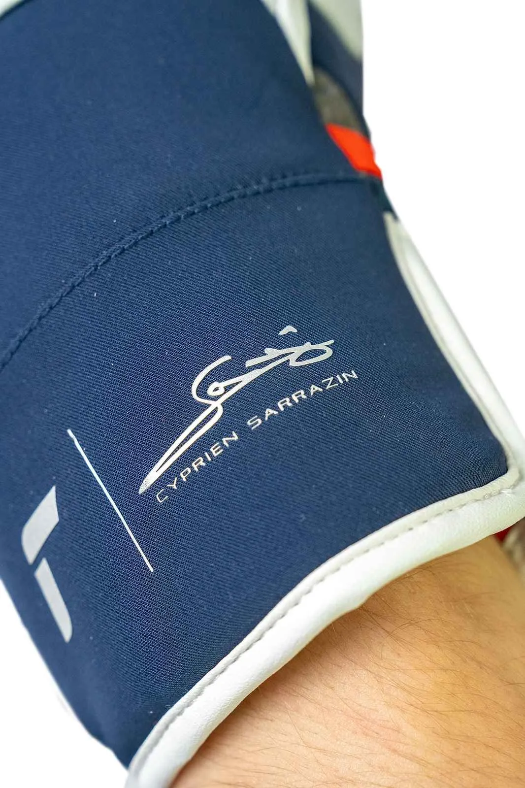 Close-up of a navy blue cuff with a white border, signed "Cyprien Sarrazin".