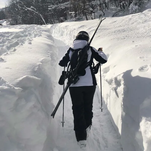 Person with skis on their back and ski pole in hand walking through the snow. Skiback is visible.
