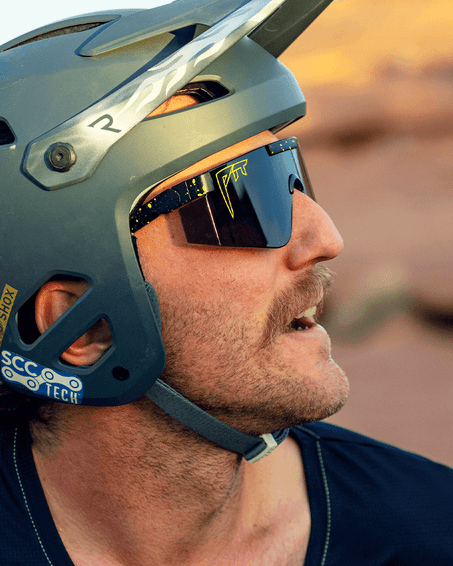 Homme avec lunettes de soleil Homme casqué portant des lunettes de soleil The Cosmos 2000 avec des éclaboussures de néon et un logo jaune.