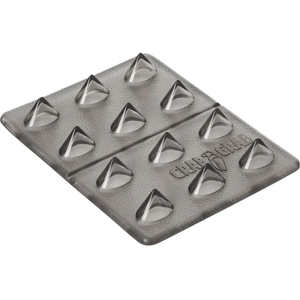 Smoke-gray, rectangular snowboard stomp pad with twelve transparent, triangular spikes in a 3x4 grid. Mini Shark Teeth protrude noticeably and offer optimal grip. The “Crab Grab” logo is subtly embossed.