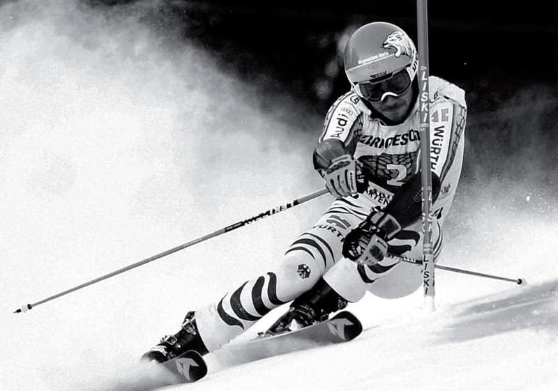 Nordica Dobermann Ski und Skischuhe Schwarzweißaufnahme eines Skirennläufers in voller Fahrt, der sich in die Kurve legt.