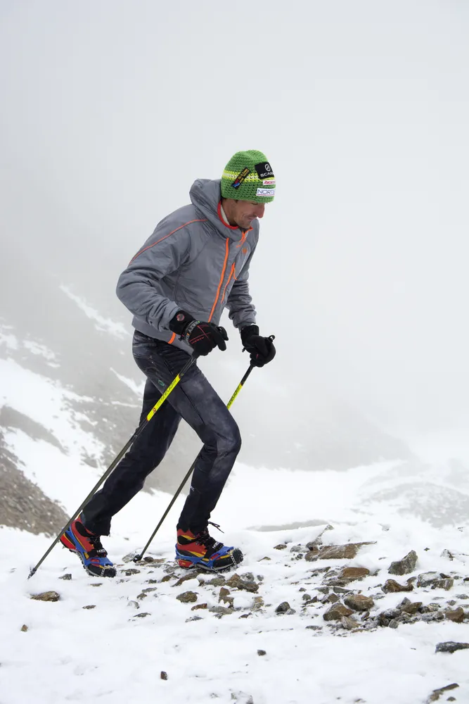 Mann mit Trekking Steigeisen und Stöcken im Schnee, Aufstieg in bergiger Landschaft.