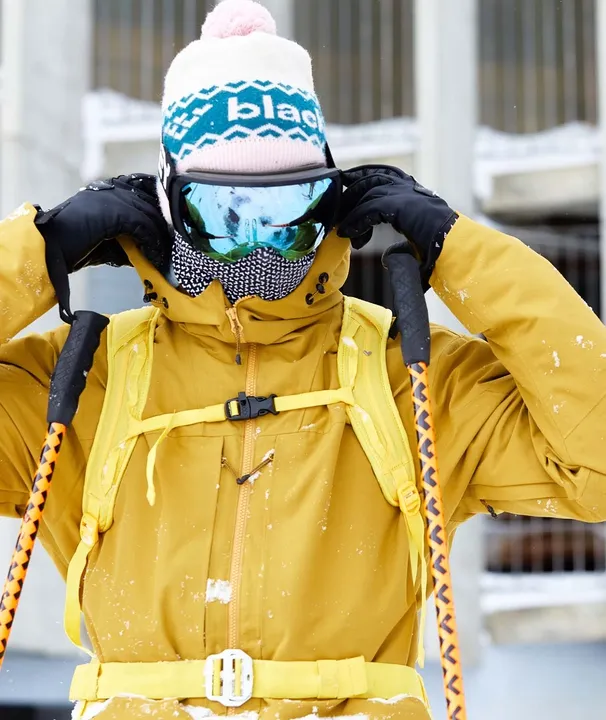 Personne en tenue de ski portant Black Crows Bonnet Crista. Le bonnet est blanc avec un motif bleu et un pompon rose.