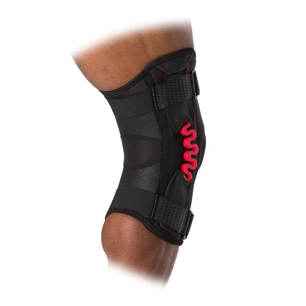 Close-up of a McDavid NRG knee support with red suspension on a person's knee. The support is black and has adjustable straps.