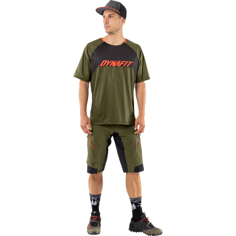 Mann in Dynafit Ride Tee Winter Moss mit Shorts, Socken und Schuhen. Das Shirt ist Grün mit Logo.