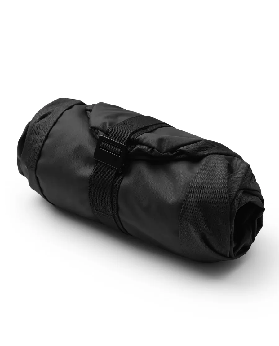 A rolled, black Db Snow Essential ski bag with a black strap in the middle.