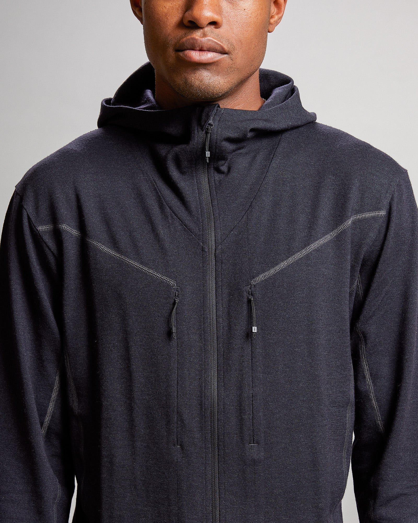 Detailaufnahme einer schwarzen Nuyarn Hood Jacket mit Reißverschluss und zwei Brusttaschen an einer Person.