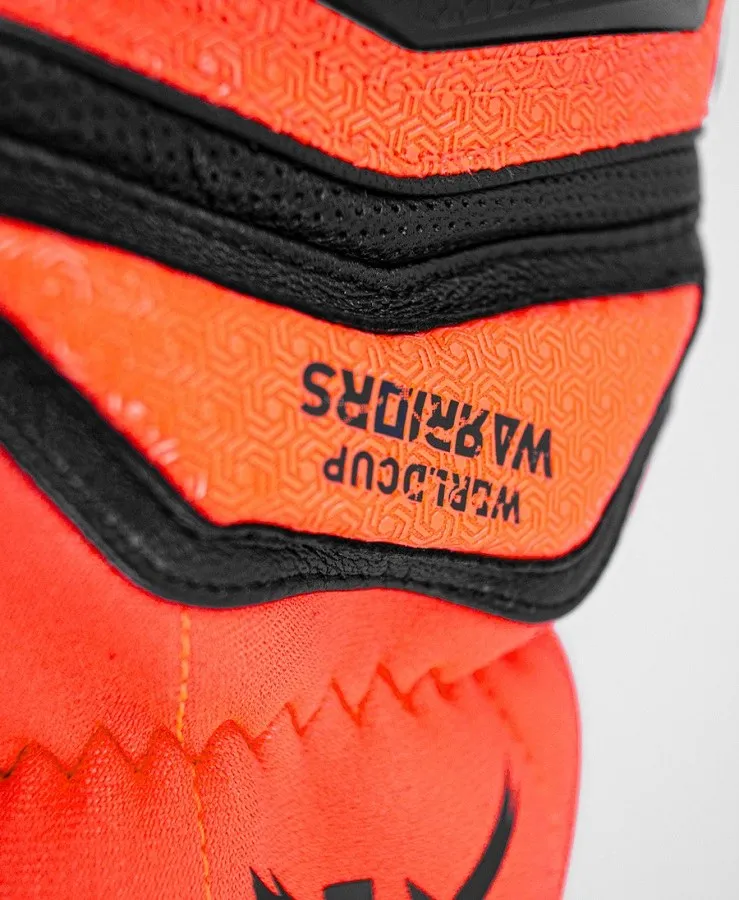 Detailed view of a Reusch Worldcup Warrior SC glove with orange pattern and black stitching. The text "WORLDCUP WARRIORS" is visible.