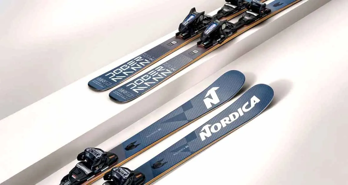 Zwei Paar Ski, eines mit "Dobermann" Aufschrift, das andere mit "Nordica", liegen auf einer weißen, stufenartigen Oberfläche.