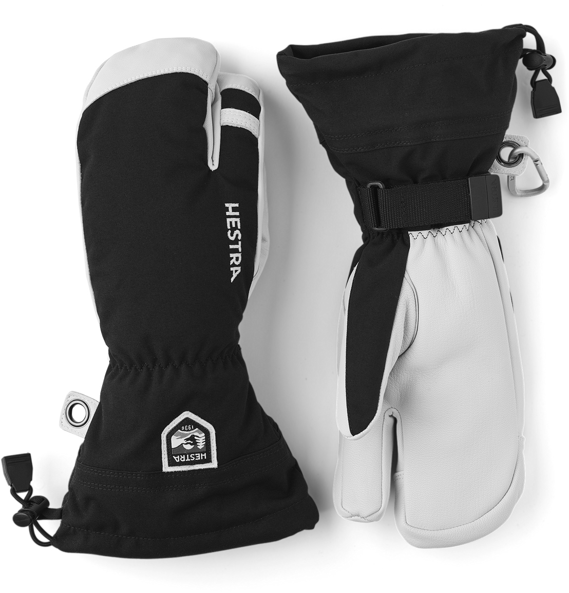 Zwei Hestra Ski-Handschuhe, ein 3-Finger-Modell, in Schwarz und Weiß, liegen nebeneinander auf weißem Untergrund.
