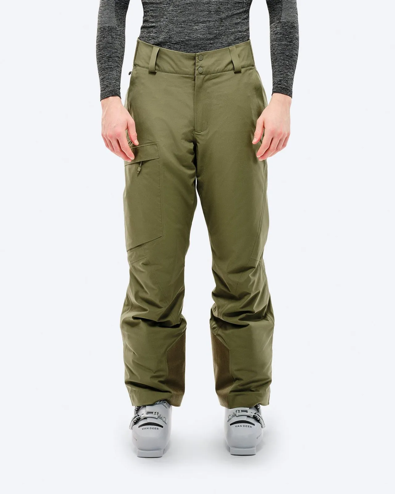 A person wears Winter Moss ski pants with ski boots in front of a white background.