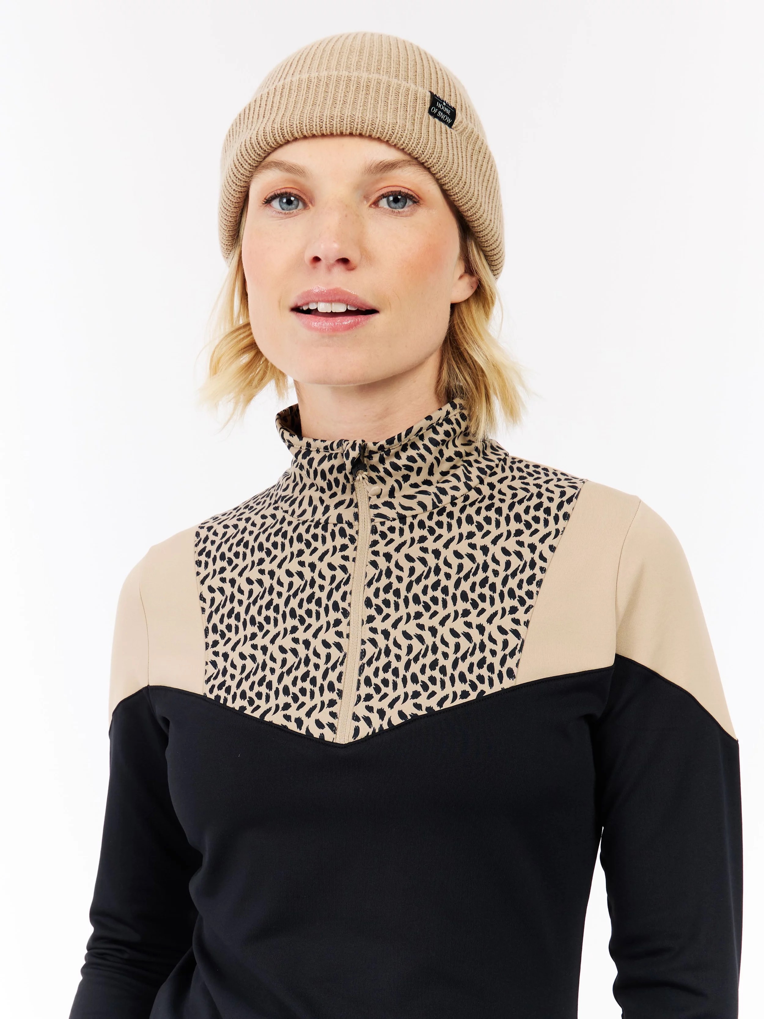 Portrait of a woman with fair skin, blue eyes and blond hair. She is wearing a beige cap and a sports top with a pattern.