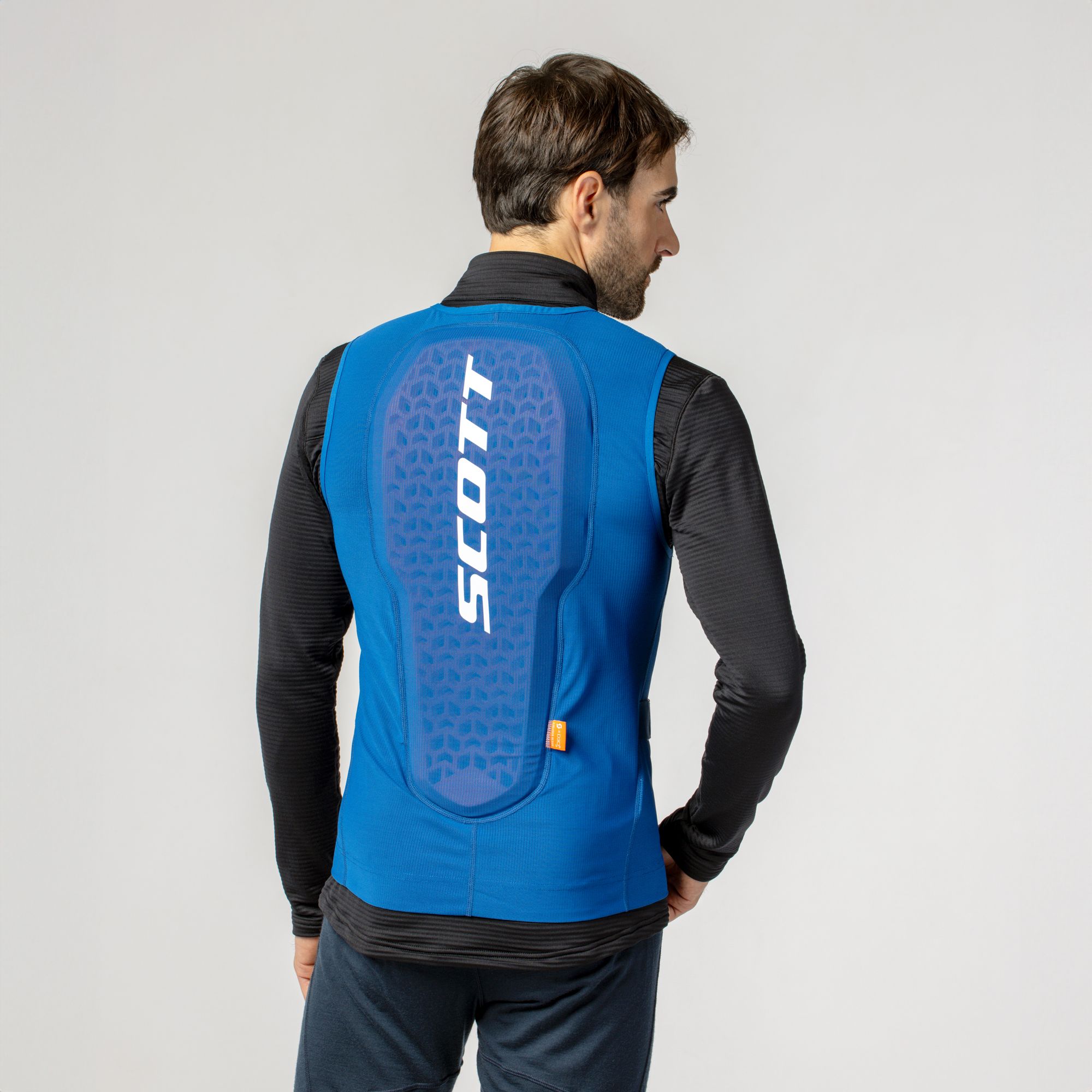 Ein Mann trägt einen blauen Scott Airflow Protektor mit großem, weißem "SCOTT" Schriftzug auf dem Rücken.