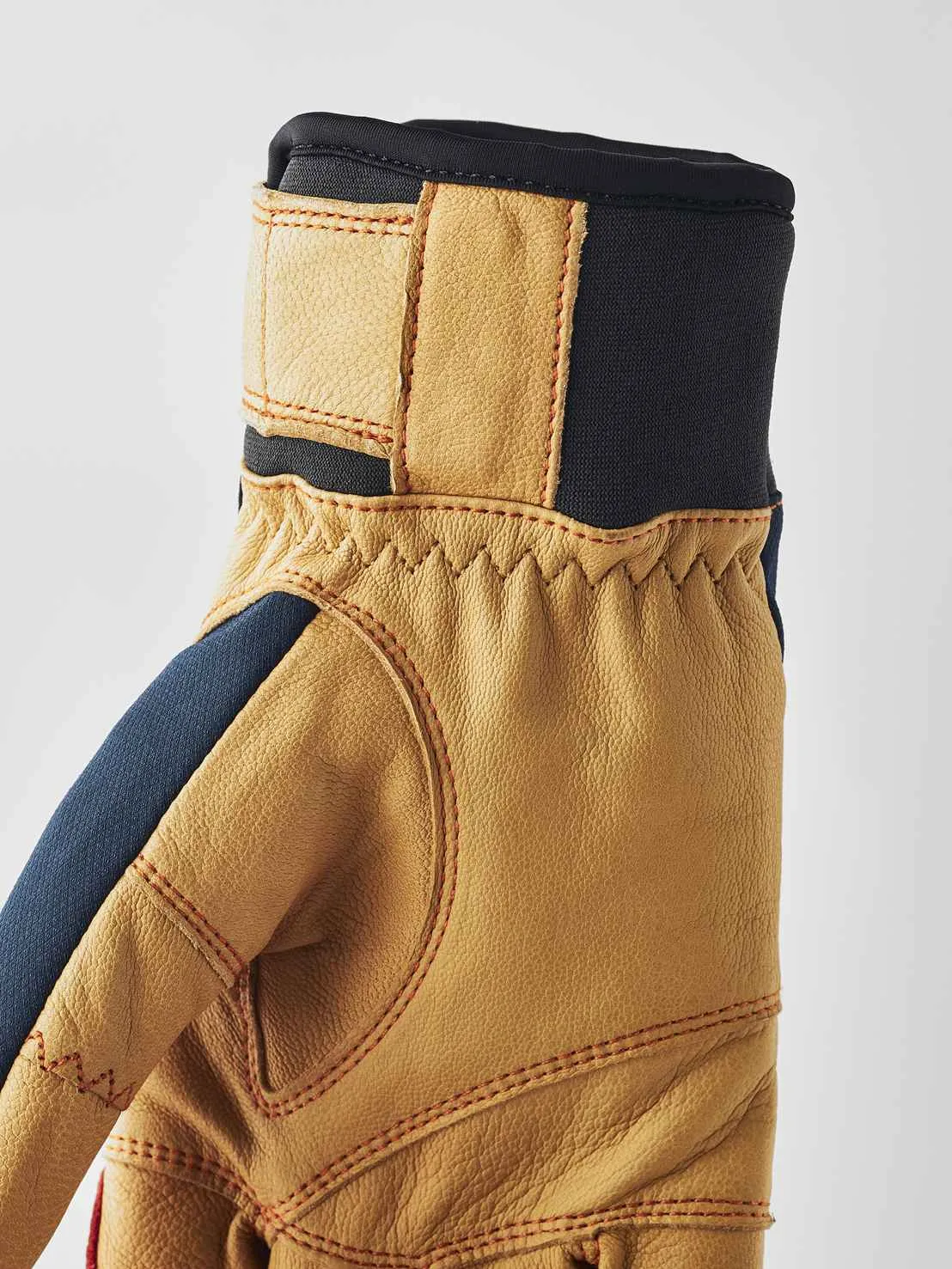 Gros plan sur un gant en cuir marron clair avec des accents bleus et des surpiqûres rouges, ainsi qu'une ceinture noire.