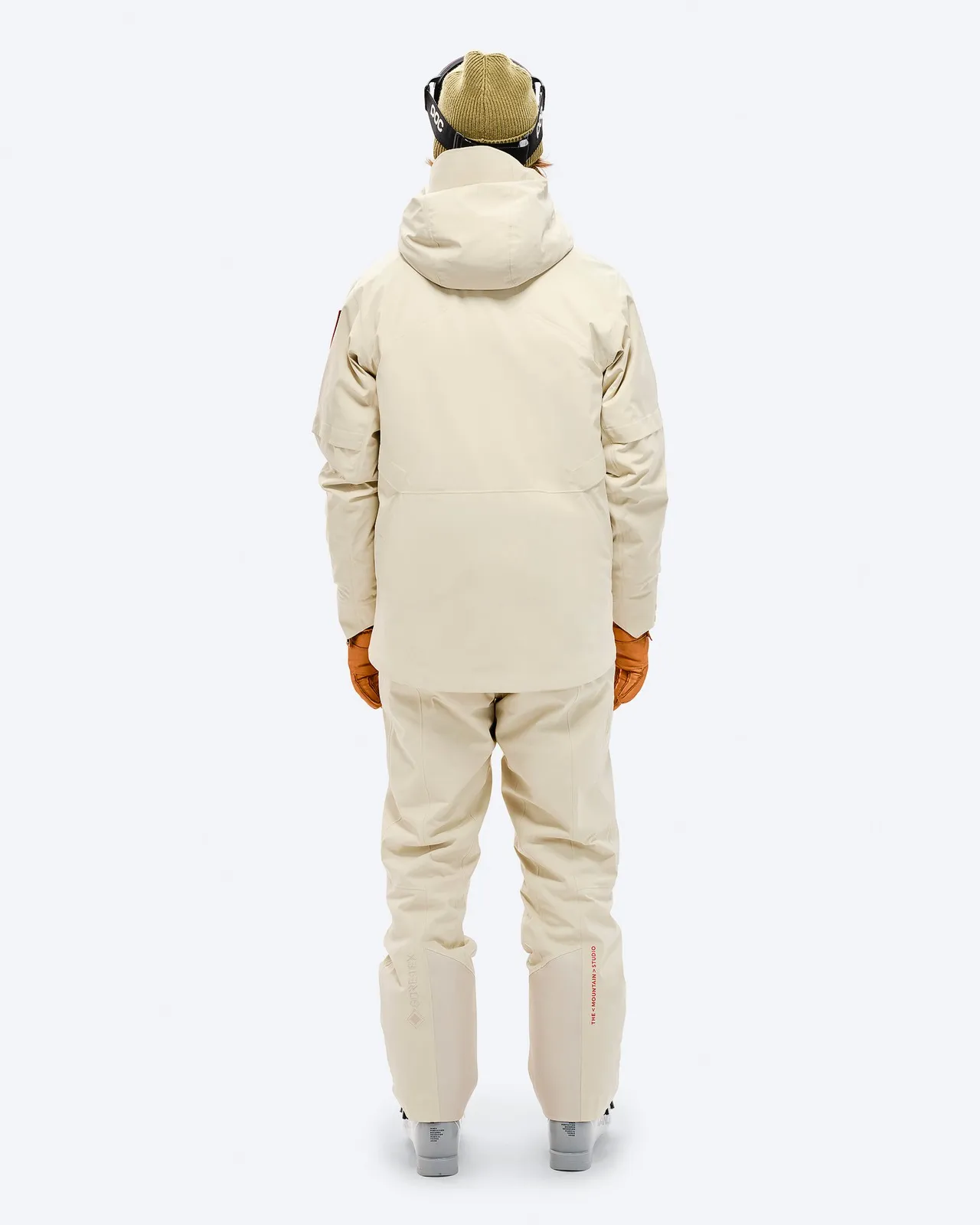 Person von hinten in beiger S-1 GORE-TEX 2L Stretch Insulated Jacke und passender Hose, braune Handschuhe, Skibrille und Mütze.